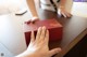 A woman is opening a red box on a table.