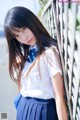 A young woman in a school uniform leaning against a fence.