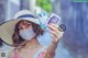 A woman wearing a hat and a face mask holding up two photos.