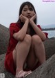 A woman in a red dress sitting on a rock by the water.