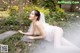 A woman in a wedding dress laying on a stone in a garden.