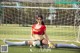 A woman sitting on the ground with a soccer ball in front of a goal.